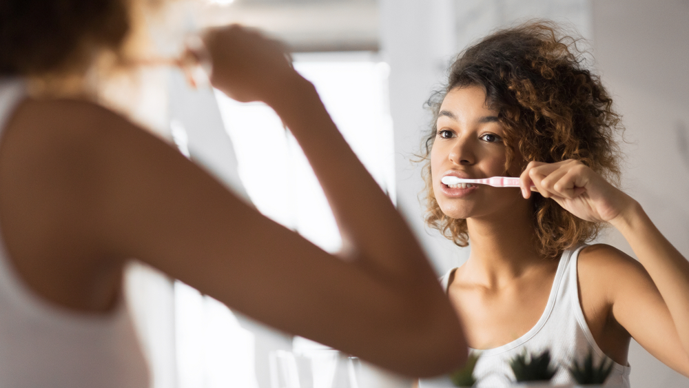 curly-haired woman brushing her teeth