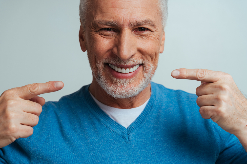 A handsome senior man pointing at his teeth - Dental Implants in Cumming