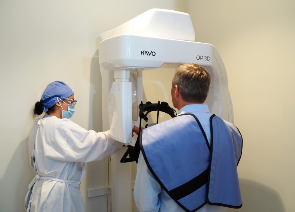 A dental professional in protective gear prepares a patient for a 3D dental X-ray scan using specialized equipment - North Atlanta Family Dentistry A dental professional in protective gear prepares a patient for a 3D dental X-ray scan using specialized equipment - North Atlanta Family Dentistry